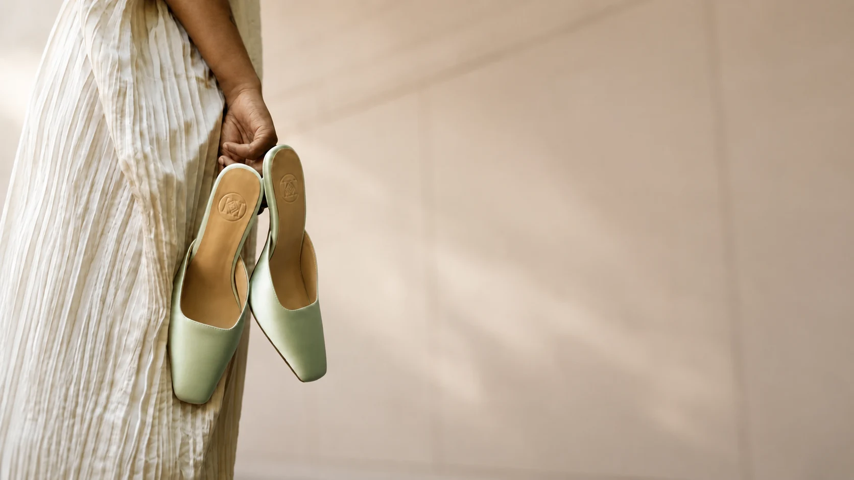 A woman holding a pair of sage-green Kahin Abri mules